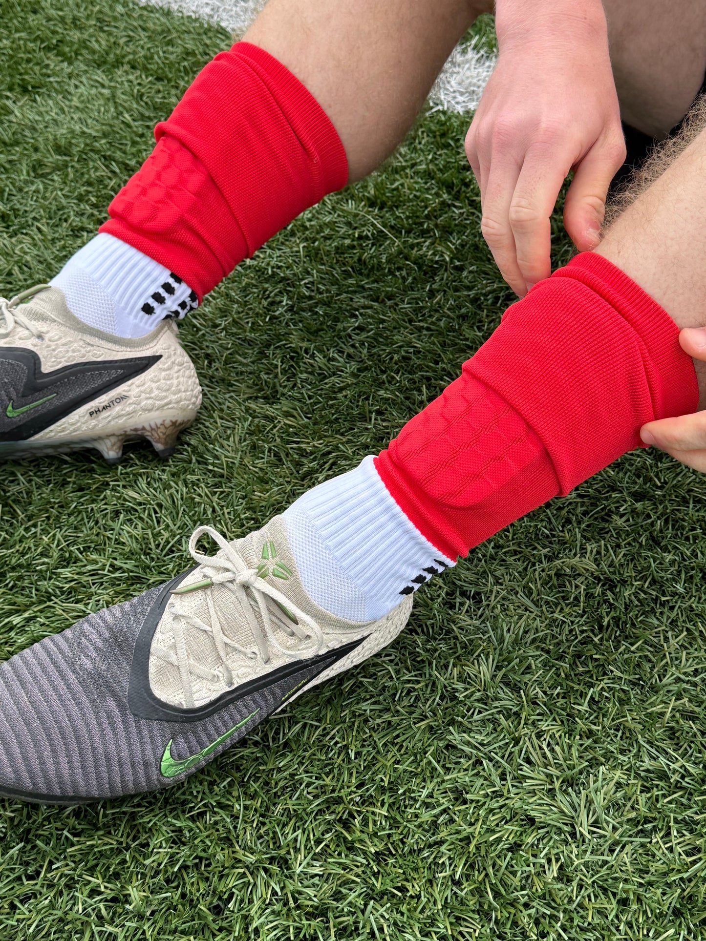 Person wearing red 3 in 1 soccer socks on a grass field